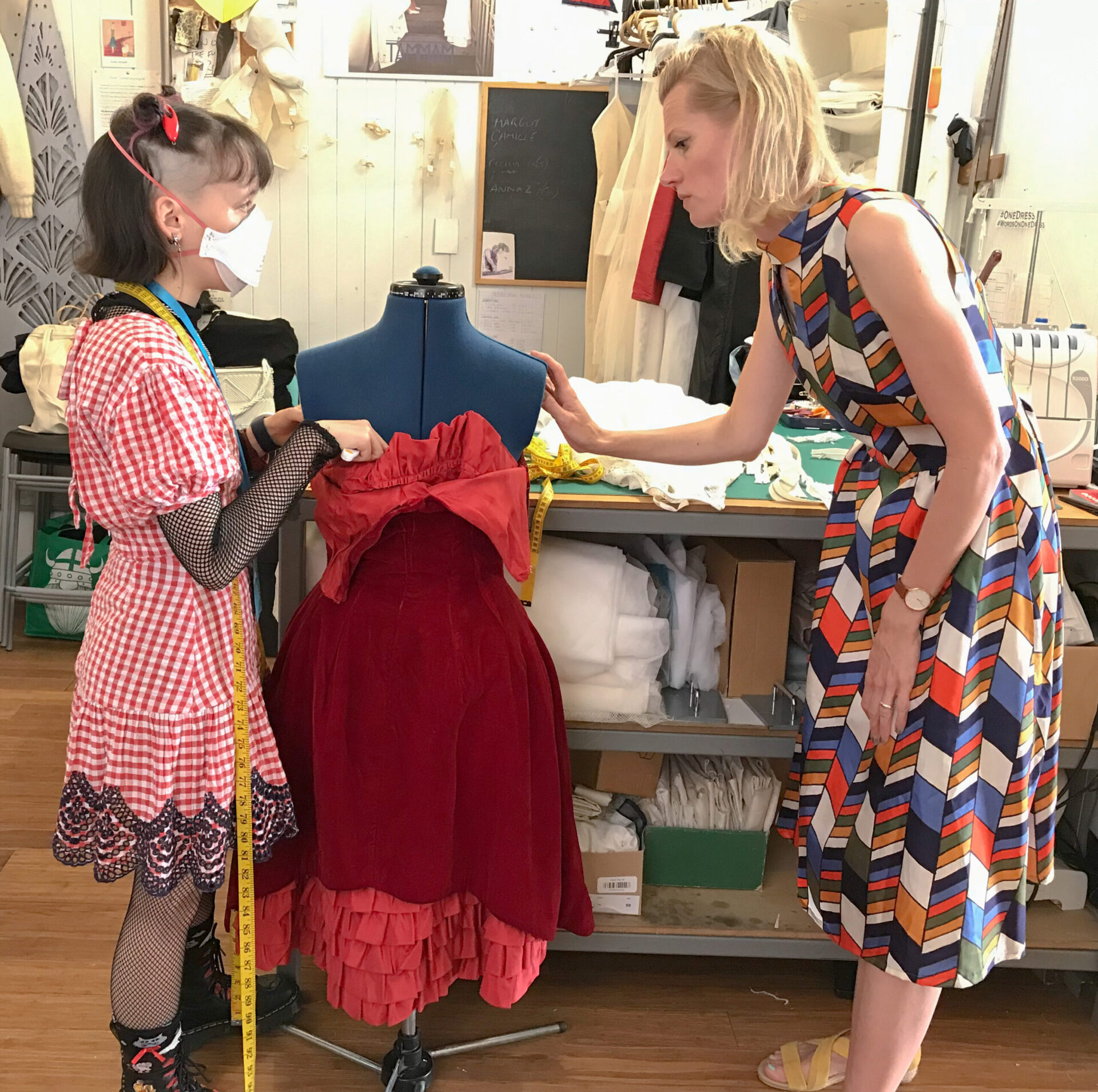 one woman teaching clothes repair services to another younger woman in a sewing workshop with a mannequin dressed in a vintage dress