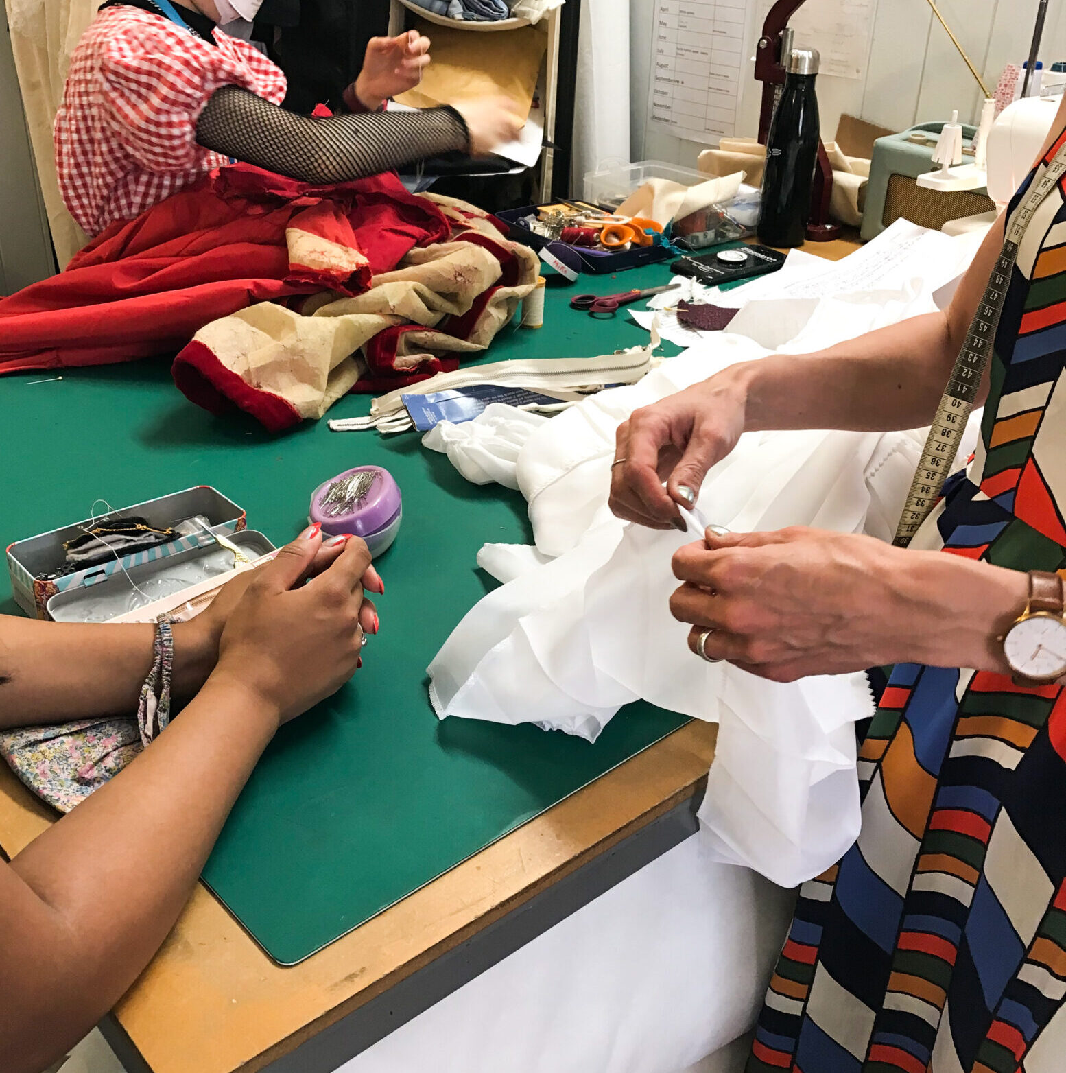 one woman teaching clothes repair services to another younger woman in a sewing workshop with a mannequin dressed in a vintage dress